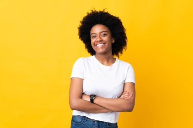 Sarı arka planda izole edilmiş genç Afrikalı Amerikalı kadın kollarını ön cephede çapraz tutuyor.