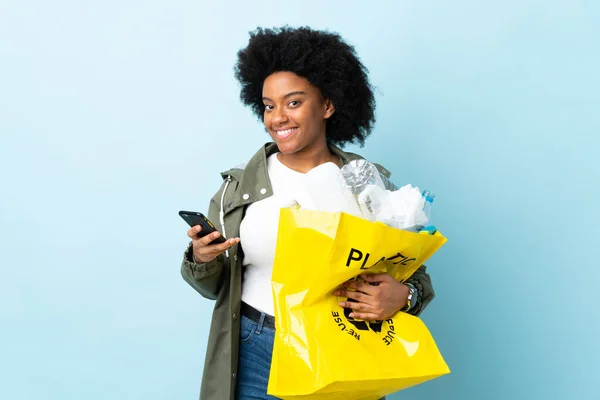 Young African American woman holding a recycle bag isolated on colorful background sending a message with the mobile