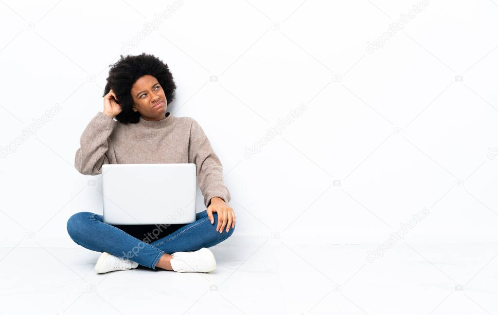 Young African American woman with a laptop sitting on the floor having doubts and with confuse face expression