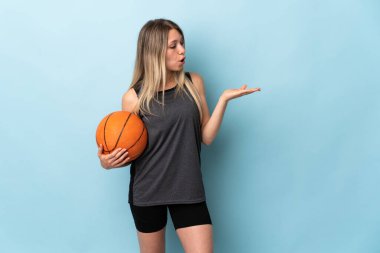 Basketbol oynayan sarışın genç bir kadın mavi arka planda izole edilmiş bir şekilde.