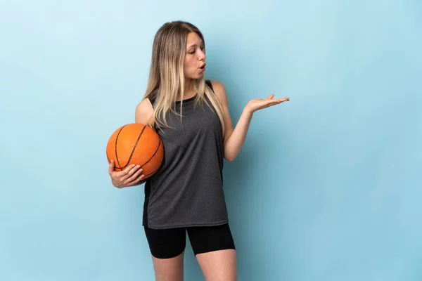 年轻的金发女子在蓝色背景下打篮球 手心拿着想象的复制空间 — 图库照片