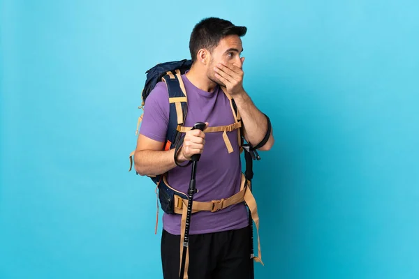 年轻的高加索人 背着背包 两根远足的杆子 被蓝色的背景隔离 嘴上覆盖着 朝侧面看去 — 图库照片