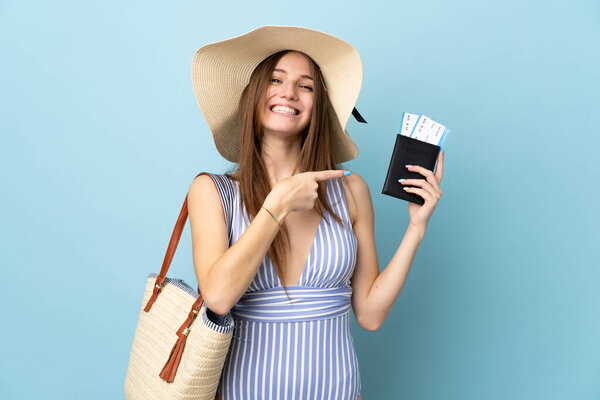 Young caucasian woman in summer holidays holding passport isolated on blue background and pointing it