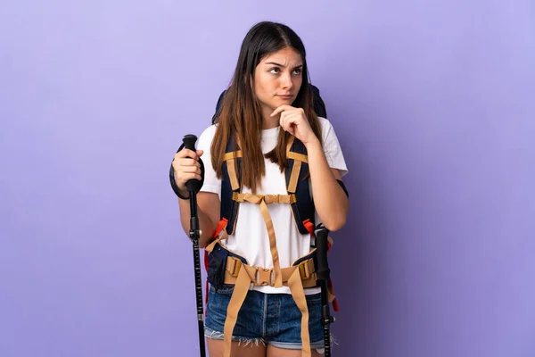 Jovem Com Mochila Postes Trekking Isolados Fundo Roxo Com Dúvidas — Fotografia de Stock