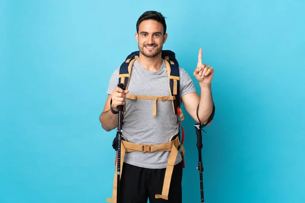 Jovem Caucasiano Com Mochila Postes Trekking Isolados Fundo Azul Apontando — Fotografia de Stock