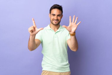 Mor arka planda izole edilmiş genç yakışıklı yediyi parmaklarıyla sayıyor