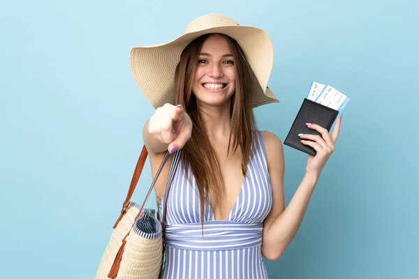 Young caucasian woman in summer holidays holding passport isolated on blue background points finger at you with a confident expression