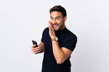 Beyaz arka planda izole edilmiş cep telefonu kullanan genç beyaz bir adam bir şeyler fısıldıyor.