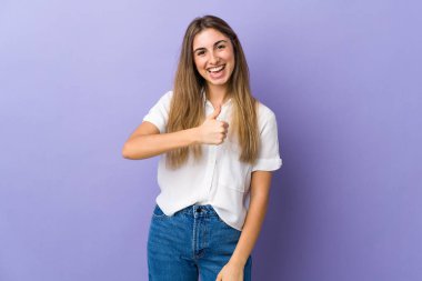 İzole edilmiş mor arka planda genç bir kadın baş parmak işareti yapıyor.