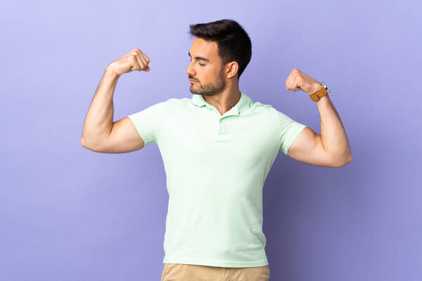 Young handsome man isolated on purple background doing strong gesture