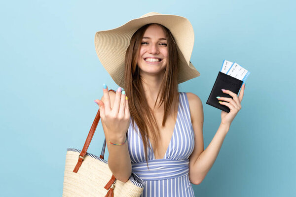 Young caucasian woman in summer holidays holding passport isolated on blue background inviting to come with hand. Happy that you came