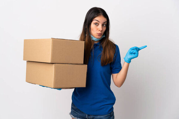Young delivery woman protecting from the coronavirus with a mask isolated on white background surprised and pointing side