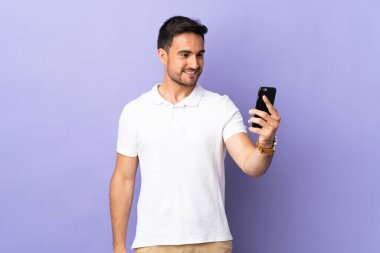 Mor arka planda izole edilmiş genç yakışıklı bir adam selfie çekiyor.