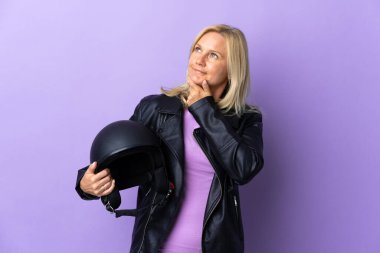 Mor arka planda izole edilmiş motosiklet kaskı tutan orta yaşlı bir kadın.