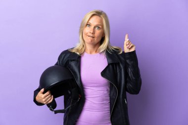 Mor arka planda izole edilmiş motosiklet kaskı tutan orta yaşlı bir kadın parmağıyla işaret eden bir fikir düşünüyor.