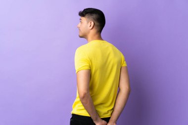 Genç Kolombiyalı adam mor arka planda izole edilmiş ve arkasına bakıyor.