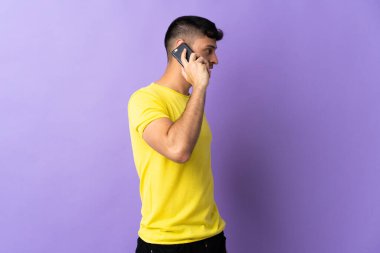 Mor arka planda izole edilmiş genç Kolombiyalı bir adam cep telefonuyla sohbet ediyor.