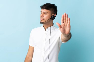 Kolombiyalı tele pazarlamacı, izole edilmiş arka planda kulaklıkla çalışıyor. Durma hareketi yapıyor ve hayal kırıklığına uğruyor.