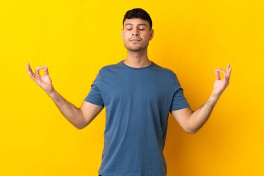 Zen pozisyonunda sarı arka planda izole genç Kolombiyalı adam