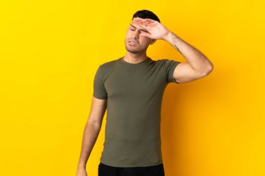 Genç Kolombiyalı adam sarı arka planda izole edilmiş, yorgun ve hasta bir ifadeyle.