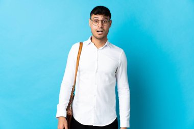 Kolombiyalı genç bir adam mavi arka planda, şaşırmış bir yüz ifadesiyle izole edilmiş.