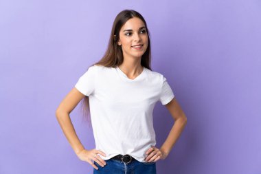 Mavi arka planda izole edilmiş genç beyaz kadın kolları kalçasında ve gülümsüyor.