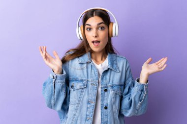 Mor arka planda izole genç beyaz kadın şaşırdı ve müzik dinliyor.