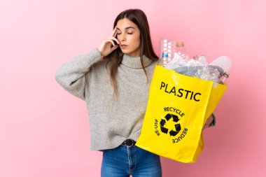 Pembe arka planda izole edilmiş, baş ağrısıyla izole edilmiş plastik şişelerle dolu bir çanta taşıyan beyaz bir kadın.