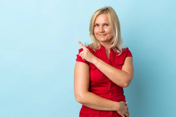 Middelbare Leeftijd Vrouw Geïsoleerd Blauwe Achtergrond Wijzend Naar Zijkant Een — Stockfoto