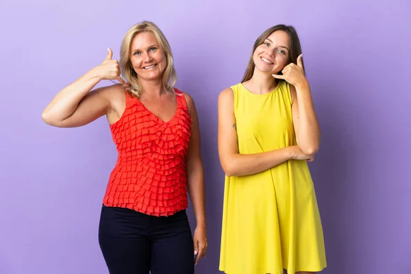 Mom and daughter isolated on purple background making phone gesture. Call me back sign