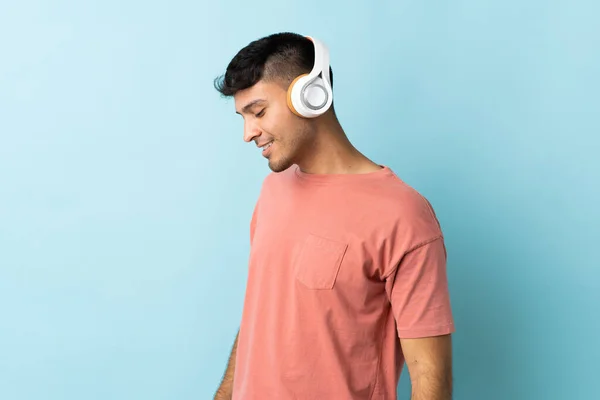 Joven Colombiano Aislado Sobre Fondo Azul Escuchando Música —  Fotos de Stock