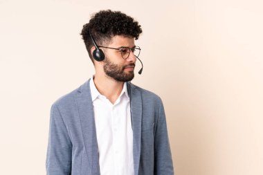 Tele pazarlamacı Faslı bir adam bej arka planda izole edilmiş bir kulaklıkla çalışıyor.