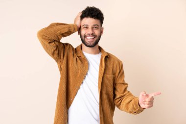 Faslı genç adam bej arka planda izole edilmiş. Şaşırmış ve parmağıyla kenarı işaret ediyor.