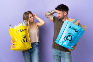 Mor arka planda izole edilmiş, kafaları kaşınırken kuşkuları olan genç beyaz bir çift geri dönüşüm yapıyor.