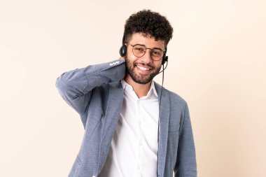 Faslı bir pazarlamacı bej arka planda izole edilmiş bir kulaklıkla çalışıyor. Gülüyor.