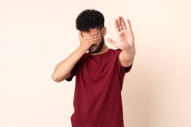 Bej arka planda izole edilmiş genç Faslı adam jesti durdurup yüzünü kapatıyor.