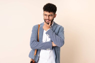 Faslı genç bir iş adamı bej arka planda izole edilmiş, yan tarafa bakıyor.