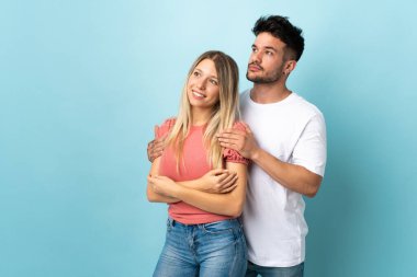 Mavi arka planda izole edilmiş genç beyaz çift yan tarafa bakıyor.