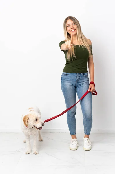 Young caucasian woman walking the dog isolated on white background showing and lifting a finger