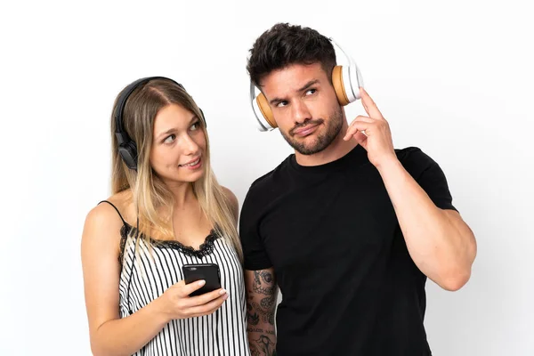 Young Caucasian Couple White Background Listening Music Mobile Thinking — Stock Photo, Image