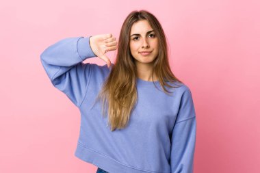 Soyutlanmış pembe arka planda genç bir kadın, olumsuz bir ifadeyle baş parmağını aşağı gösteriyor.