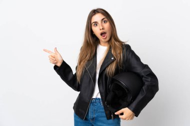 İzole edilmiş beyaz arka planda motosiklet kaskı tutan genç kadın şaşırdı ve parmağını yana çevirdi.