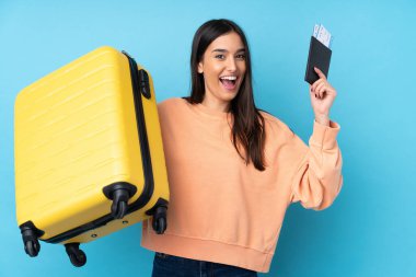 Genç esmer kadın izole edilmiş mavi arka planda tatilde bavul ve pasaportla
