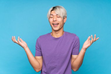 Soyutlanmış mavi arka planda genç Asyalı adam çok fazla gülümsüyor.