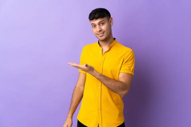 Mor arka planda izole edilmiş genç Kolombiyalı bir adam gülümserken bir fikir sunuyor.