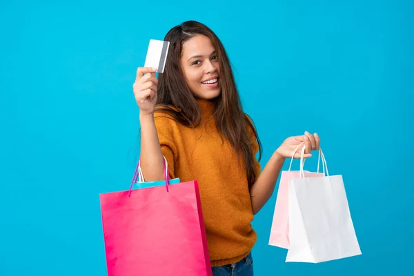 若いですブラジルの女の子以上隔離された青の背景保持ショッピングバッグとクレジットカード — ストック写真