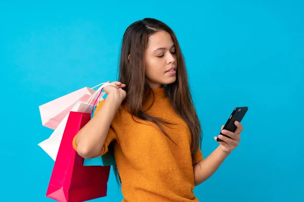 若いですブラジルの女の子以上隔離された青の背景保持ショッピングバッグと書き込みメッセージとともに彼女の携帯電話に友人 — ストック写真