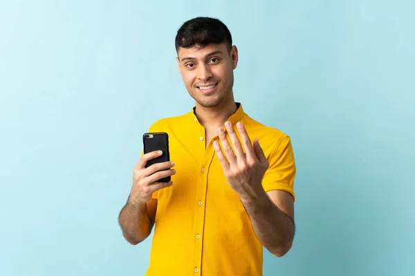 Junge Kolumbianische Mann Mit Handy Isoliert Blauen Hintergrund Einladend Mit — Stockfoto