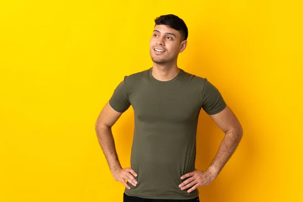 Young Colombian Man Isolated Yellow Background Posing Arms Hip Smiling — Stock Photo, Image