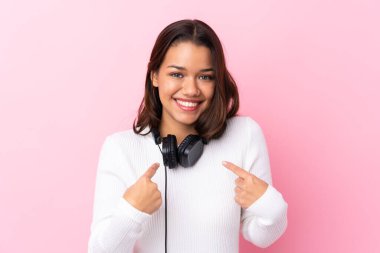 Kulaklıklı genç bir kadın. Yüzünde sürpriz bir ifade olan izole pembe bir duvarın üzerinde.